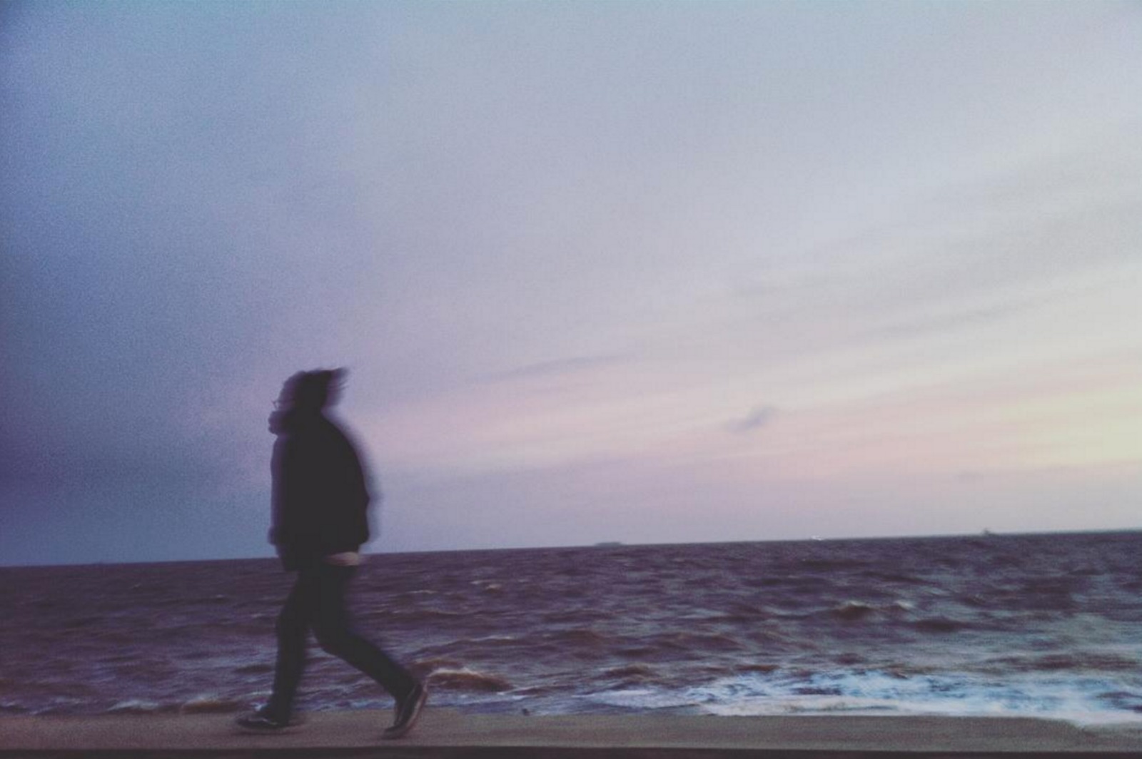 Silueta de una persona caminando sola junto al mar, al atardecer
