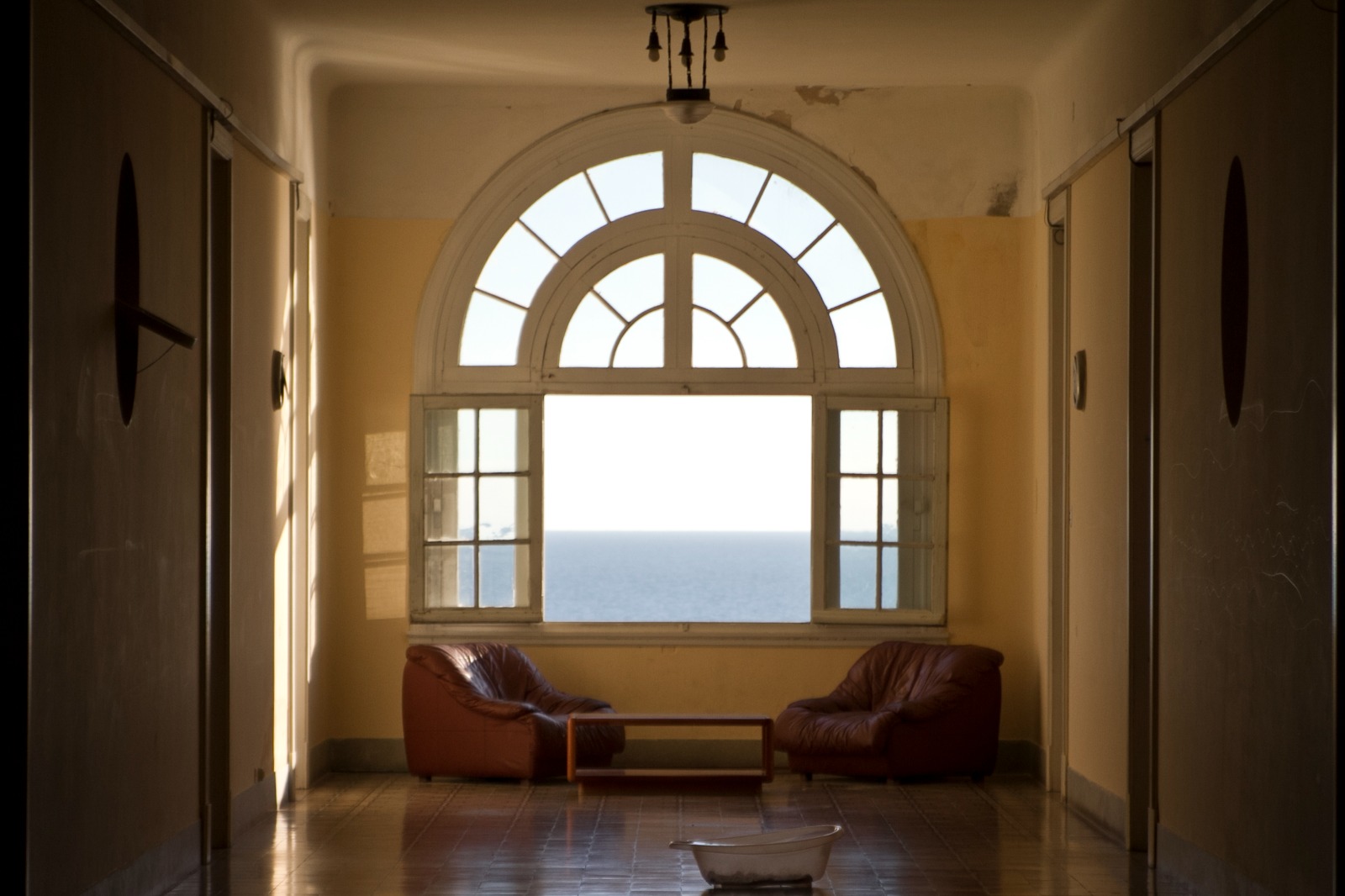 Pasillo con ventana en arco y vista al mar, con dos sillones de espera